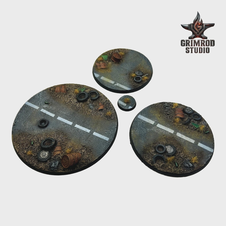 May include: A set of four circular miniature bases depicting a post-apocalyptic road scene. The bases feature a gray asphalt road with a white center line, scattered debris, tires, and barrels. The Grimrod Studio logo is in the upper right corner.