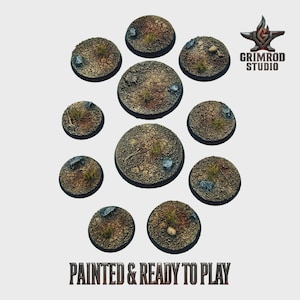 May include: A collection of ten circular, textured bases for miniature figures. The bases are painted with a desert-like terrain, featuring cracked earth, small rocks, and patches of dry grass. The text "PAINTED & READY TO PLAY" is visible.