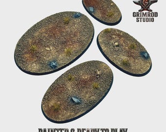 May include: Four oval-shaped miniature bases with a textured, desert-like terrain. The bases are painted with brown, tan, and green hues, featuring small tufts of grass and scattered rocks. The text "PAINTED & READY TO PLAY" is at the bottom.