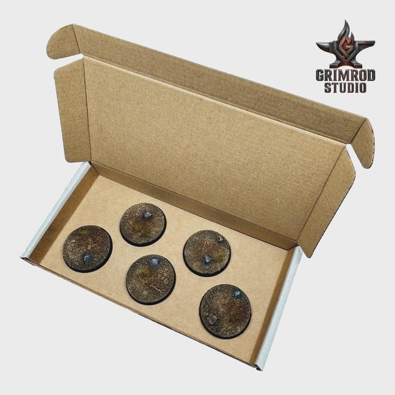 May include: A cardboard box containing five round, textured bases for miniature figures. The bases are brown with patches of green and small, metallic accents. The Grimrod Studio logo is visible in the upper right corner.