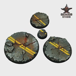 May include: Four circular bases with a cracked asphalt design, featuring yellow road lines. The bases vary in size, with the largest measuring approximately 2 inches in diameter. The Grimrod Studio logo is in the upper right corner.