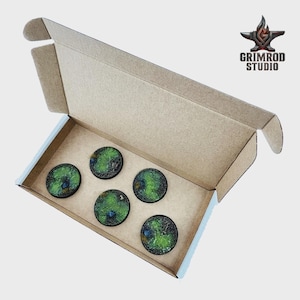 May include: An open cardboard box containing five circular, textured bases with green and black details. The bases are arranged inside the box. The Grimrod Studio logo is visible in the upper right corner.