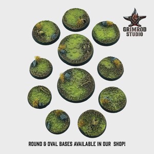 May include: A collection of round and oval miniature bases with a grassy, textured surface. Each base features patches of green, yellow, and brown, with small rocks and bone details. The bases are arranged on a light background. Text reads "ROUND & OVAL BASES AVAILABLE IN OUR SHOP!"