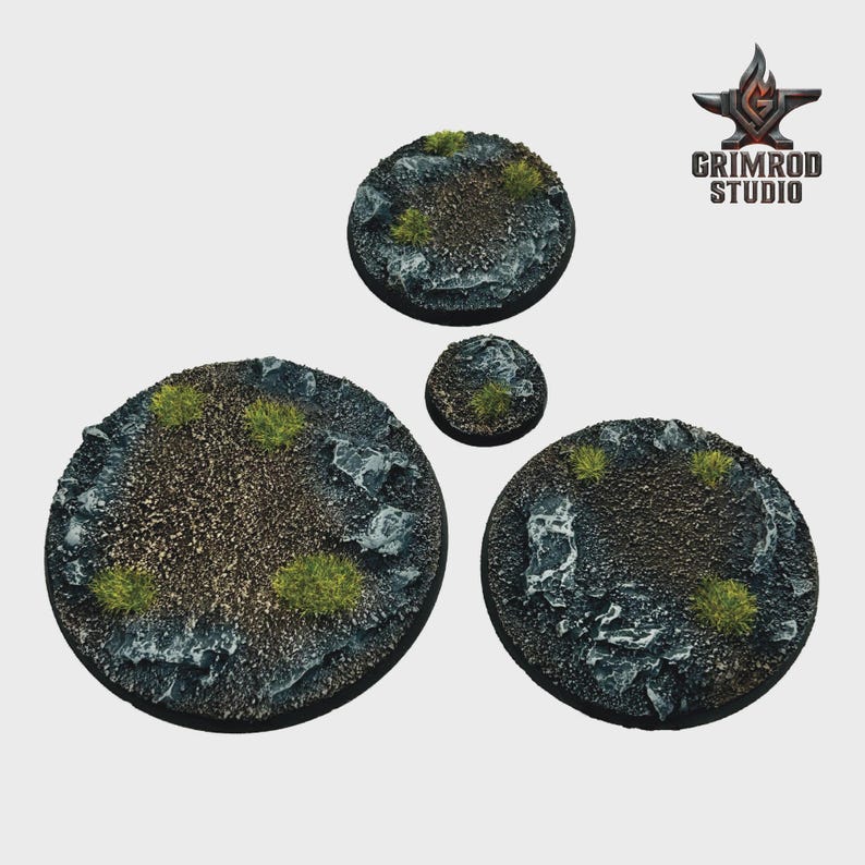 May include: Four circular miniature bases with a textured, rocky surface and patches of green vegetation. The bases vary in size, with the largest measuring approximately 2 inches in diameter. The Grimrod Studio logo is in the upper right corner.