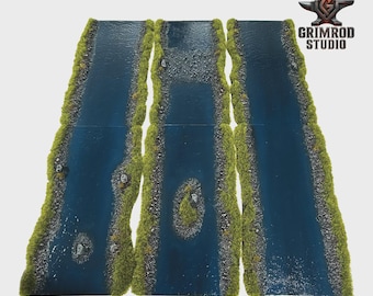 May include: Three rectangular tabletop gaming river terrain sections featuring dark blue water, textured rocky banks, and vibrant green grass flocking. The center section includes a small island, while the outer sections feature scattered rocks.