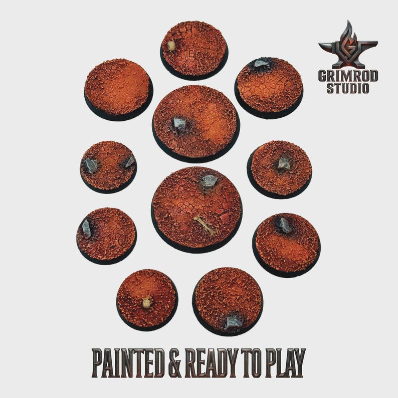 May include: A collection of eleven round, textured bases, painted in shades of brown and orange, with small rock details. The bases are arranged in a circular pattern. The text "PAINTED & READY TO PLAY" is at the bottom.