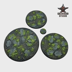 May include: Four circular miniature bases with a textured, rocky surface. The bases are painted in shades of gray, green, and brown, with detailed rock and moss elements. The Grimrod Studio logo is in the upper right corner.