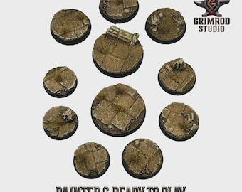 May include: A collection of ten circular, textured bases, painted in shades of brown and tan, with patches of green. The bases are designed to look like a stone surface with grass and debris. The text "PAINTED & READY TO PLAY" is visible.