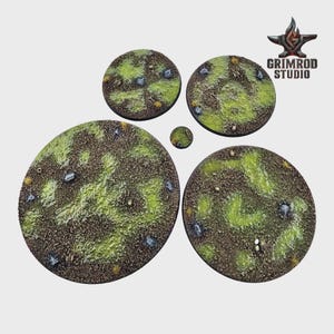 May include: A collection of five circular miniature bases with textured surfaces. The bases feature a mix of brown, green, and gray tones, with small rocks and patches of grass. The Grimrod Studio logo is visible in the upper right corner.