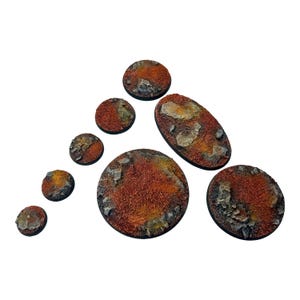 May include: A selection of seven miniature terrain bases in various shapes, including circles and an oval. The bases have a textured, reddish-brown surface with rock-like details, ideal for tabletop gaming.