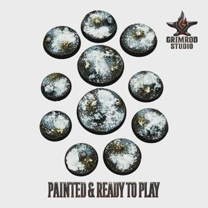 May include: Eleven circular miniature bases with a textured finish, painted to resemble snow and grass. The bases feature white and green hues. The text "PAINTED & READY TO PLAY" is visible at the bottom of the image.