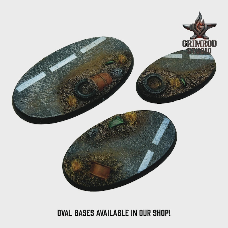 May include: Three oval-shaped miniature bases with a road surface design. Each base features a gray asphalt texture with white lane markings, debris, and a tire. The bases are designed for miniature figures. The text "OVAL BASES AVAILABLE IN OUR SHOP!" is at the bottom.