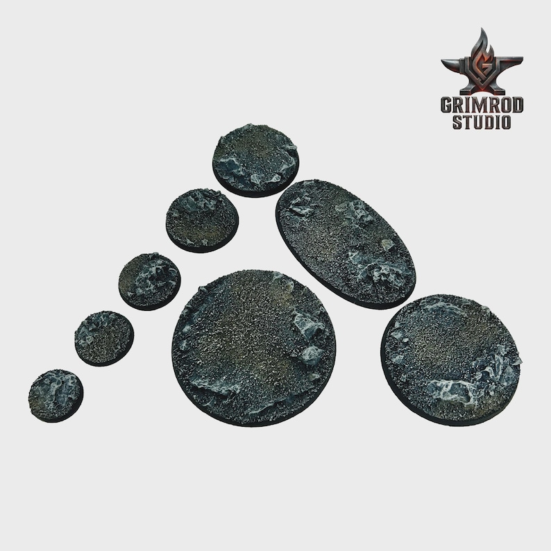 May include: A collection of textured, gray miniature bases in various shapes and sizes. The bases have a rough, rocky appearance, with a mix of dark and light gray tones. The Grimrod Studio logo is in the upper right corner.