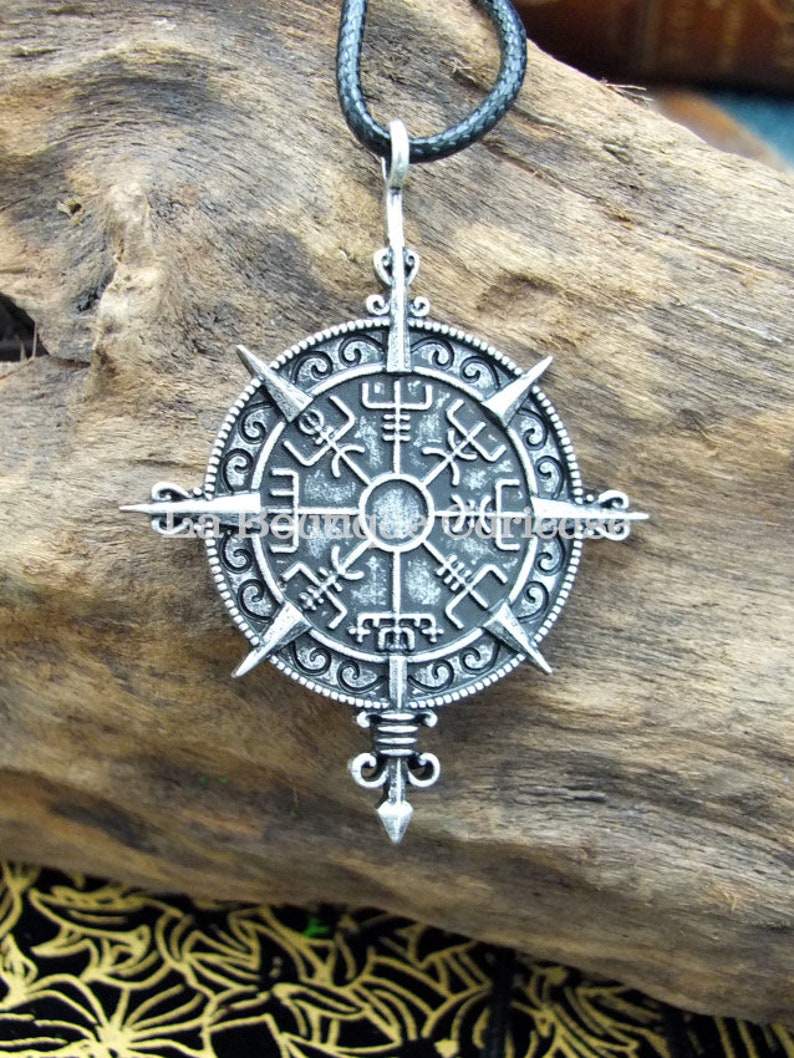 May include: A silver-toned pendant necklace with a compass design featuring Norse runes. The pendant is attached to a black cord.