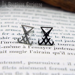 May include: Two silver earrings featuring a black sigil design. The sigil is a triangle with a line through it and a circle at the top.