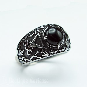 Peut inclure: Une bague en onyx noir avec une bande en argent ornée d'un motif complexe de pentagramme et de motifs floraux.