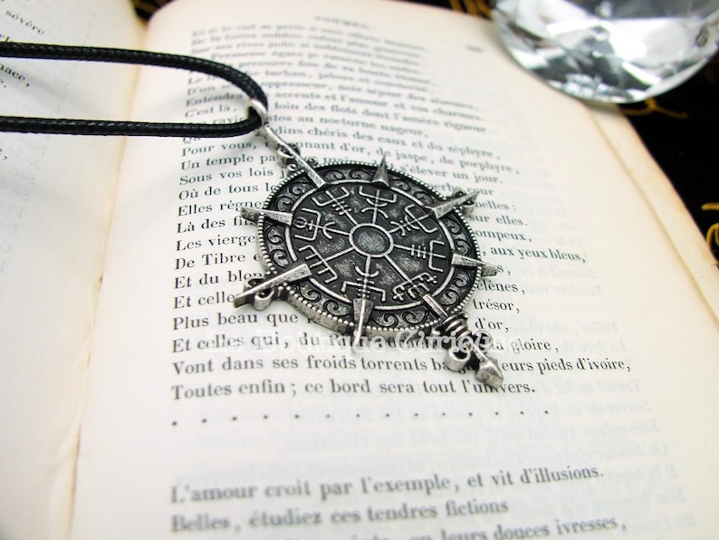 May include: A silver compass pendant necklace with a black leather cord. The compass features a circular design with a star in the center and runes around the edge.