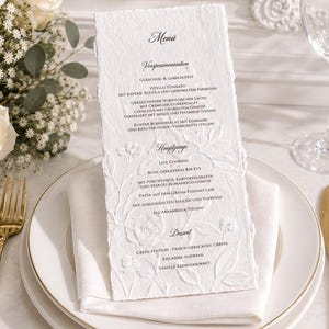 Gepersonaliseerde menukaart met blinddruk op handgemaakt of katoenpapier – elegante tafeldecoratie voor bruiloften en exclusieve evenementen.