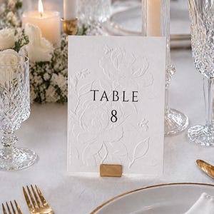 Minimalistische und elegante Tischnummern für Hochzeit & Event auf hochwertigem handgeschöpftem Büttenpapier in Weiß oder Ivory. Veredelt mit floraler Blindprägung und edlem Digitaldruck, wählbar in 3 stilvollen Farben. Die Fine-Art Tischkarten schaffen eine luxuriöse und zeitlose Tischdekoration für moderne Hochzeiten, Dinner, Gala oder exklusive Feiern. Ideal für Brautpaare, die elegante Papeterie, hochwertige Hochzeitsdeko und individuelles Design lieben.