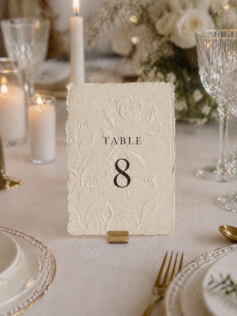 Minimalistische und elegante Tischnummern für Hochzeit & Event auf hochwertigem handgeschöpftem Büttenpapier in Weiß oder Ivory. Veredelt mit floraler Blindprägung und edlem Digitaldruck, wählbar in 3 stilvollen Farben. Die Fine-Art Tischkarten schaffen eine luxuriöse und zeitlose Tischdekoration für moderne Hochzeiten, Dinner, Gala oder exklusive Feiern. Ideal für Brautpaare, die elegante Papeterie, hochwertige Hochzeitsdeko und individuelles Design lieben.