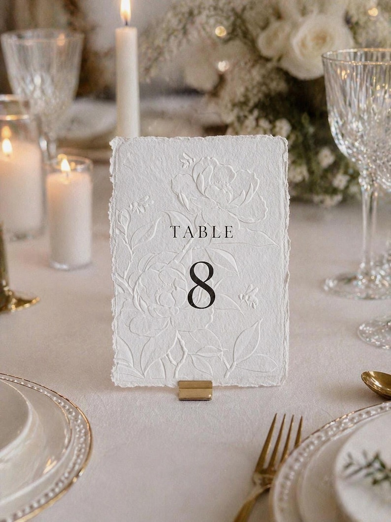 Minimalistische und elegante Tischnummern für Hochzeit & Event auf hochwertigem handgeschöpftem Büttenpapier in Weiß oder Ivory. Veredelt mit floraler Blindprägung und edlem Digitaldruck, wählbar in 3 stilvollen Farben. Die Fine-Art Tischkarten schaffen eine luxuriöse und zeitlose Tischdekoration für moderne Hochzeiten, Dinner, Gala oder exklusive Feiern. Ideal für Brautpaare, die elegante Papeterie, hochwertige Hochzeitsdeko und individuelles Design lieben.