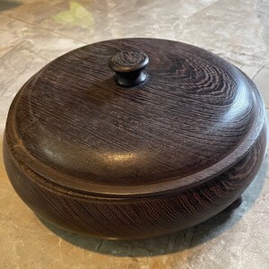 May include: A dark brown wooden box with a lid and a knob on top. The box has a rounded shape and sits on four small feet.