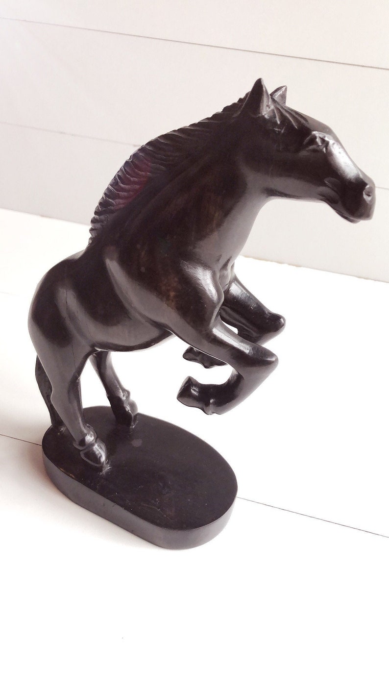 Puede incluir: Una escultura de caballo marr&oacute;n oscuro en pose encabritada. El caballo est&aacute; tallado en un material s&oacute;lido y se apoya sobre una base ovalada. La crin y los detalles est&aacute;n finamente tallados, mostrando la forma musculosa del caballo. Es un objeto decorativo.