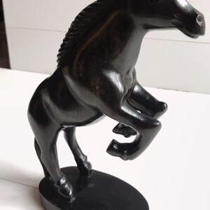 Puede incluir: Escultura de caballo negro de madera en pose encabritada. El caballo est&aacute; sobre una base ovalada negra, con un acabado liso y brillante. La escultura tiene detalles, incluyendo una melena fluida y forma musculosa, sobre un fondo blanco.