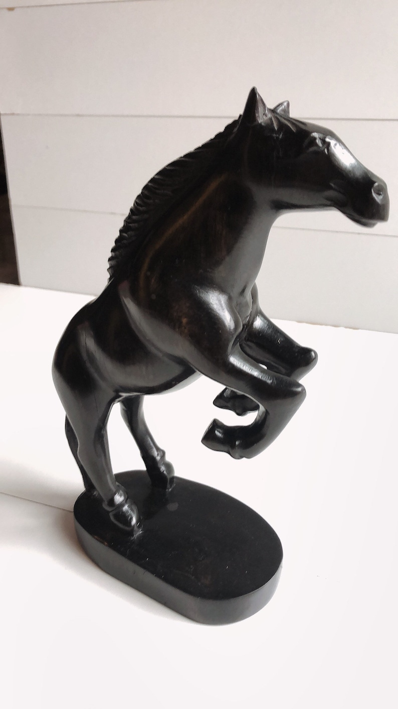 Puede incluir: Escultura de caballo negro de madera en pose encabritada. El caballo est&aacute; sobre una base ovalada negra, con un acabado liso y brillante. La escultura tiene detalles, incluyendo una melena fluida y forma musculosa, sobre un fondo blanco.