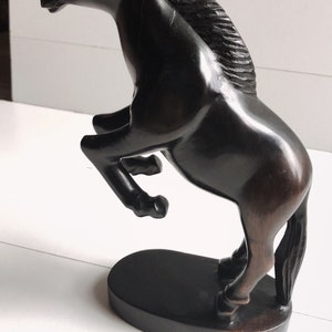 Puede incluir: Escultura de caballo marr&oacute;n oscuro en pose encabritada. El caballo est&aacute; tallado con detalles, incluyendo una melena fluida y un cuerpo musculoso. Se apoya sobre una base ovalada oscura, creando una pieza decorativa din&aacute;mica y elegante.