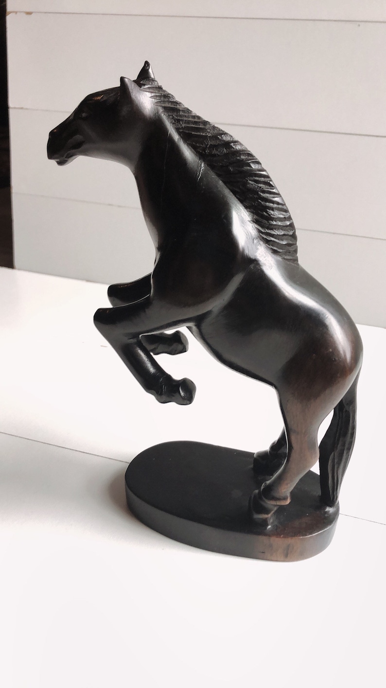 Puede incluir: Escultura de caballo marr&oacute;n oscuro en pose encabritada. El caballo est&aacute; tallado con detalles, incluyendo una melena fluida y un cuerpo musculoso. Se apoya sobre una base ovalada oscura, creando una pieza decorativa din&aacute;mica y elegante.
