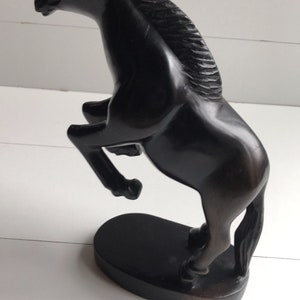 Puede incluir: Escultura de un caballo marr&oacute;n oscuro en pose de encabritado. El caballo est&aacute; tallado con detalles, incluyendo una melena fluida y un cuerpo musculoso. La escultura est&aacute; montada sobre una base ovalada oscura.