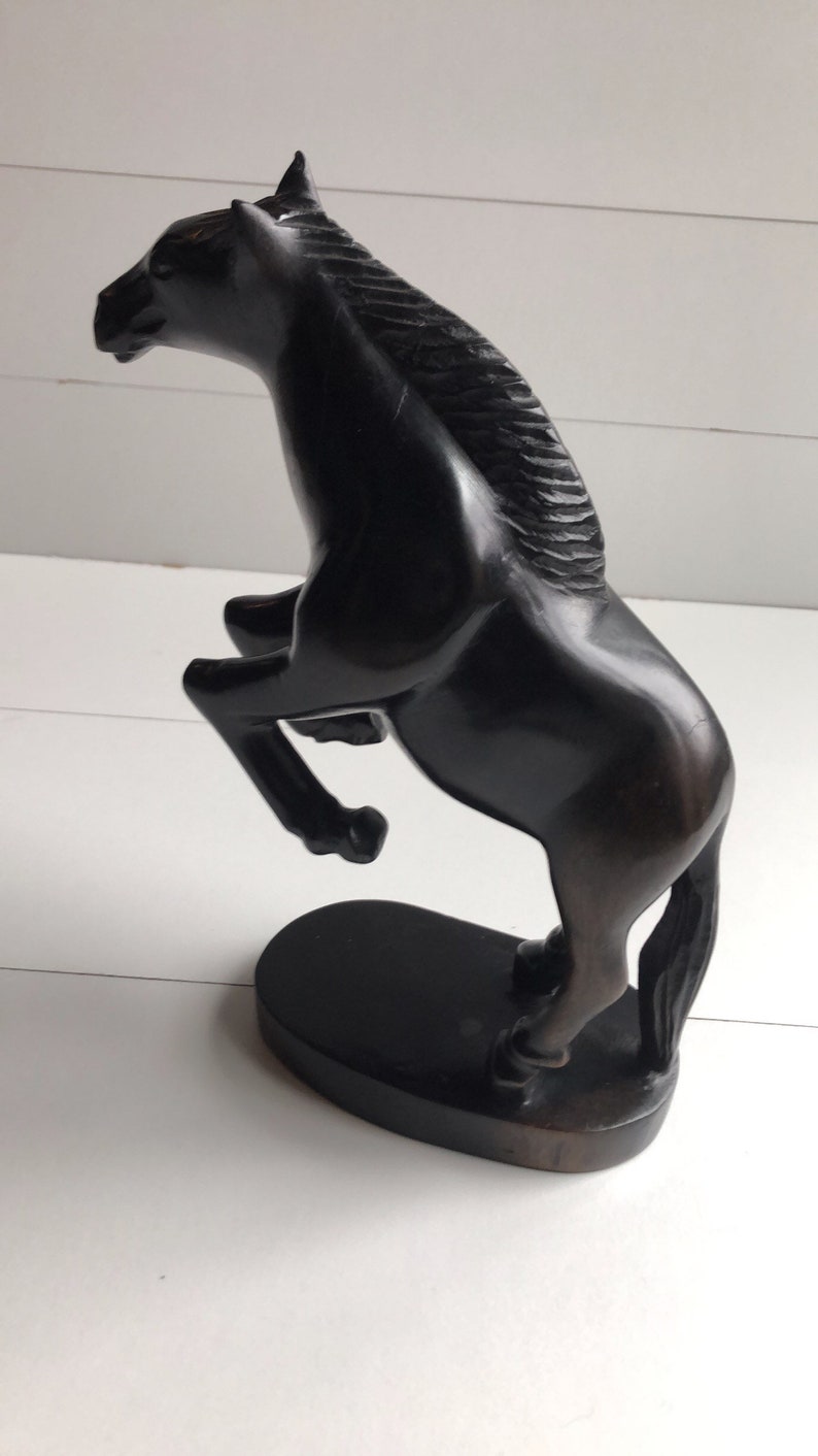 Puede incluir: Escultura de un caballo marr&oacute;n oscuro en pose de encabritado. El caballo est&aacute; tallado con detalles, incluyendo una melena fluida y un cuerpo musculoso. La escultura est&aacute; montada sobre una base ovalada oscura.