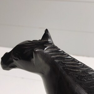 Puede incluir: Escultura de caballo negro, tallada en madera, con detalles en la melena y rasgos faciales. La escultura se encuentra sobre un fondo blanco, resaltando el color oscuro y el dise&ntilde;o intrincado. Un art&iacute;culo decorativo.