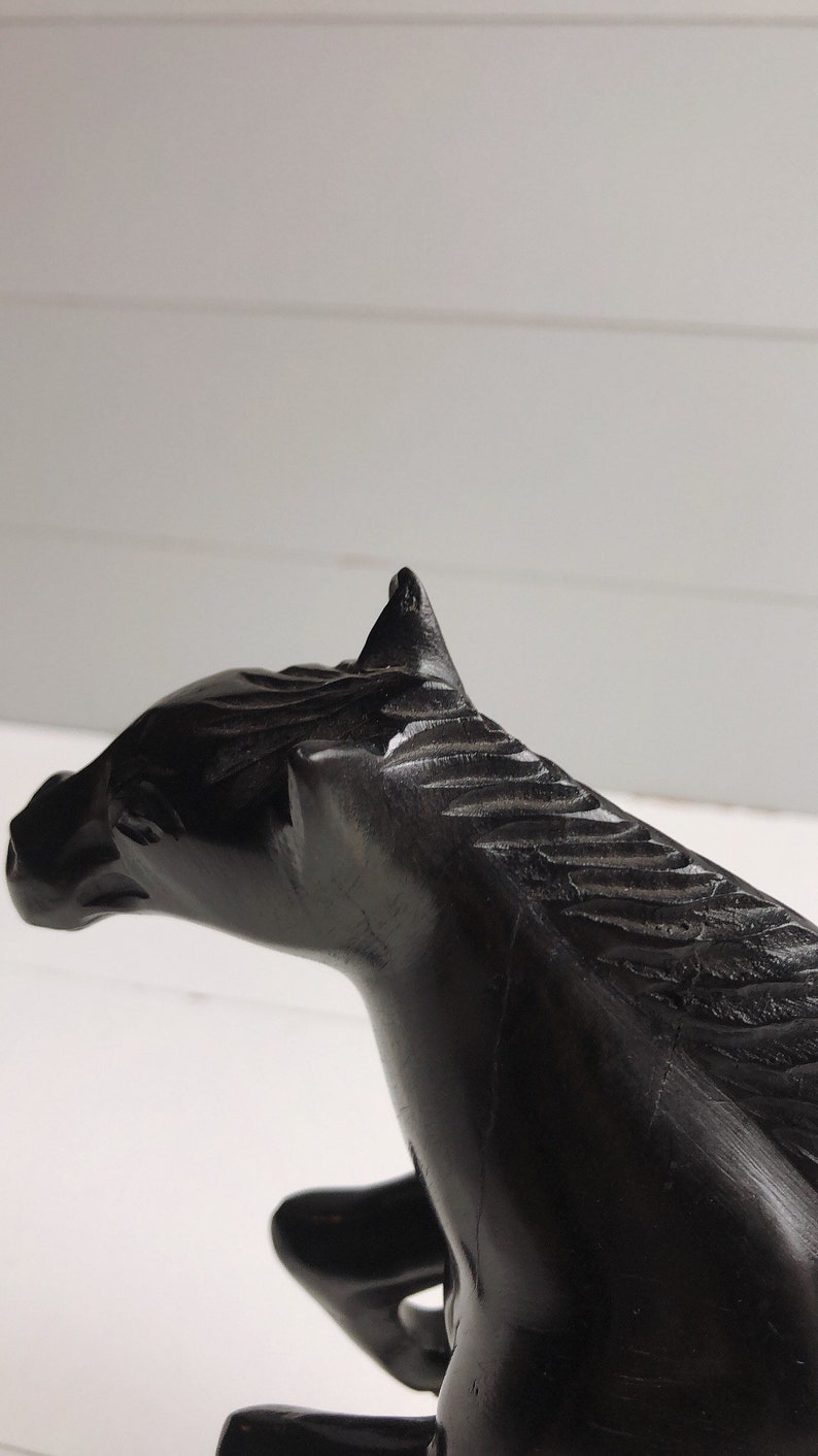 Puede incluir: Escultura de caballo negro, tallada en madera, con detalles en la melena y rasgos faciales. La escultura se encuentra sobre un fondo blanco, resaltando el color oscuro y el dise&ntilde;o intrincado. Un art&iacute;culo decorativo.