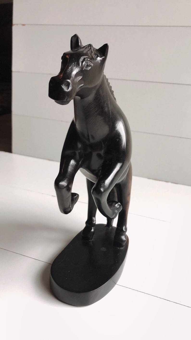 Puede incluir: Escultura de caballo de madera negra en pose de encabritado. El caballo est&aacute; sobre una base ovalada negra. La escultura tiene un acabado brillante y se exhibe sobre una superficie blanca.