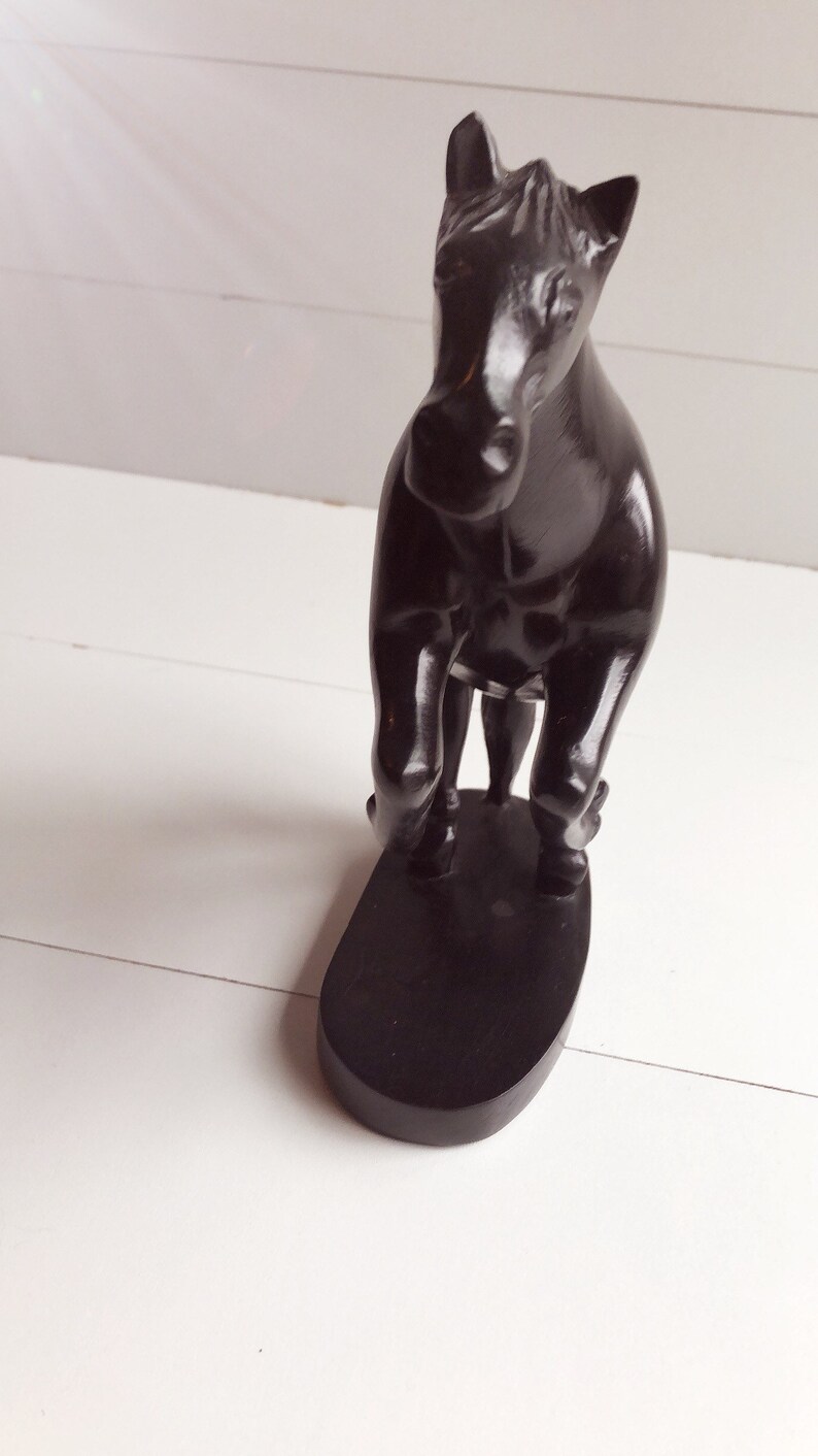 Puede incluir: Figura de caballo negro de madera. El caballo est&aacute; sobre una base ovalada negra. La figura tiene un acabado liso y brillante. El fondo es blanco.