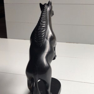 Puede incluir: Una estatua de caballo negro en posici&oacute;n encabritada. La escultura est&aacute; hecha de un material oscuro, posiblemente madera, con un acabado liso y pulido. El caballo se alza sobre una base rectangular, y la crin est&aacute; detallada con l&iacute;neas talladas.