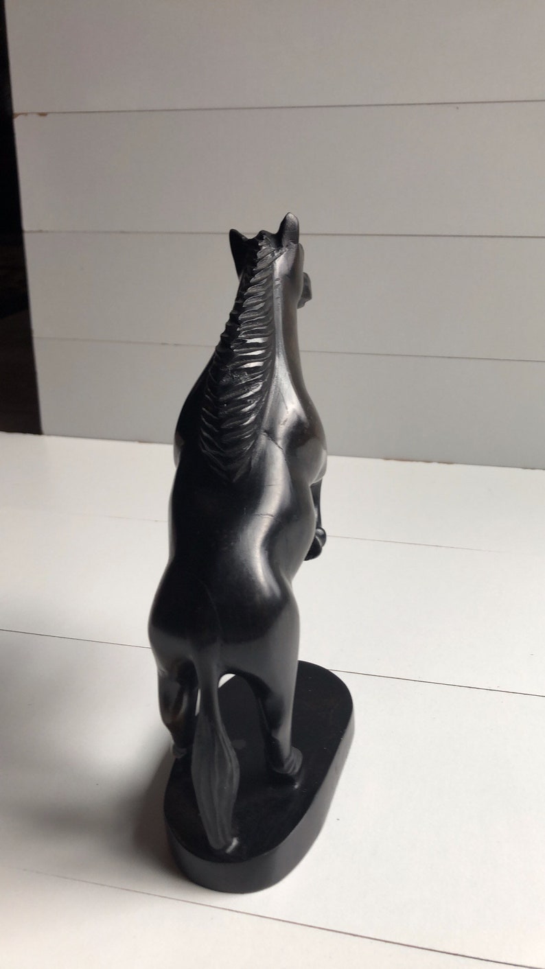 Puede incluir: Una estatua de caballo negro en posici&oacute;n encabritada. La escultura est&aacute; hecha de un material oscuro, posiblemente madera, con un acabado liso y pulido. El caballo se alza sobre una base rectangular, y la crin est&aacute; detallada con l&iacute;neas talladas.