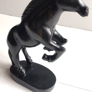 Puede incluir: Figura de caballo negro en pose de encabritado. La escultura est&aacute; hecha de un material oscuro, posiblemente madera, y est&aacute; montada sobre una base ovalada. La melena y el cuerpo del caballo est&aacute;n detallados, y el dise&ntilde;o es elegante.