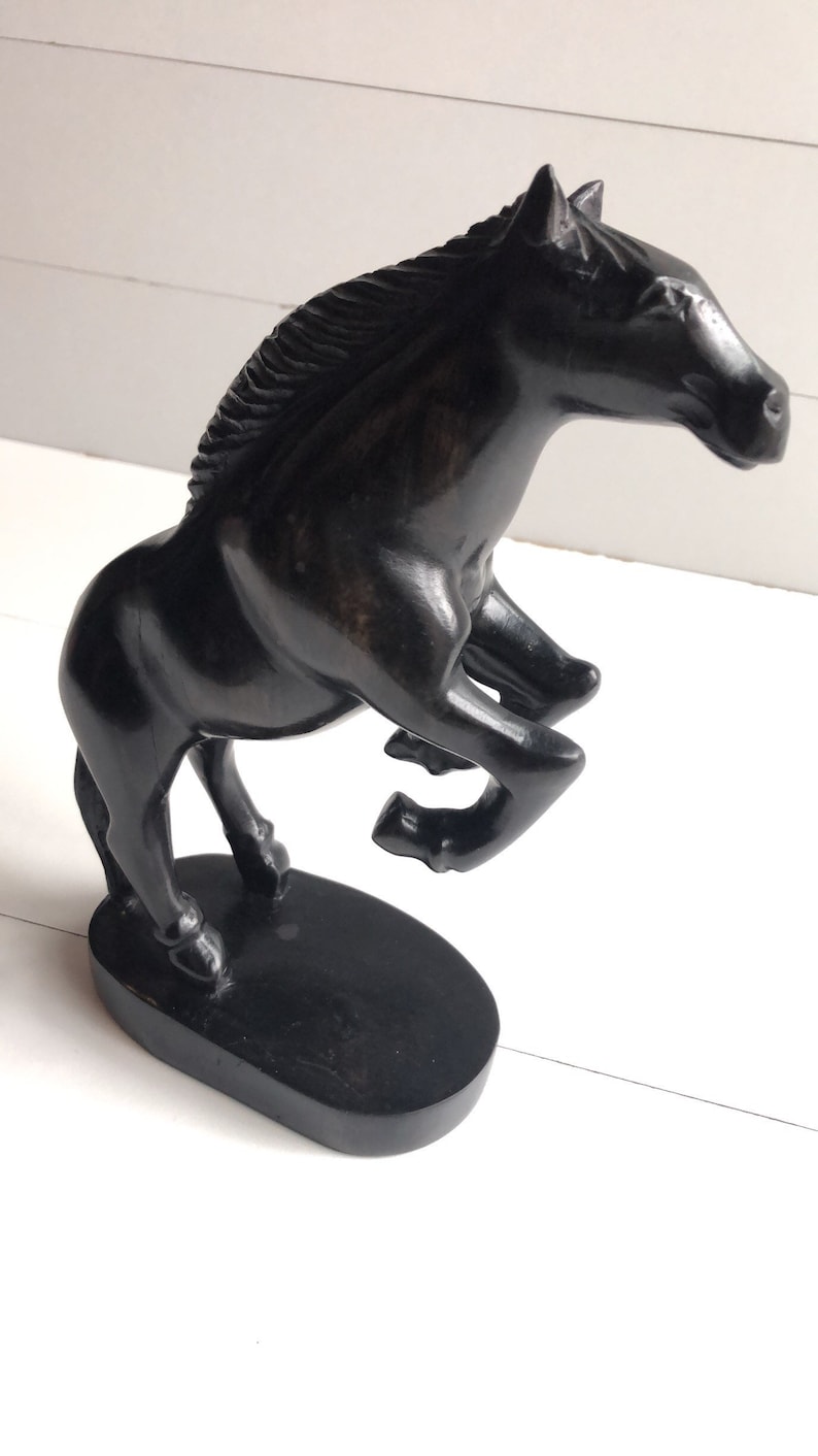 Puede incluir: Figura de caballo negro en pose de encabritado. La escultura est&aacute; hecha de un material oscuro, posiblemente madera, y est&aacute; montada sobre una base ovalada. La melena y el cuerpo del caballo est&aacute;n detallados, y el dise&ntilde;o es elegante.