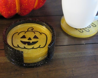 May include: A set of four gold glitter coasters with a black glitter rim. The top coaster features a black silhouette of a jack-o'-lantern.