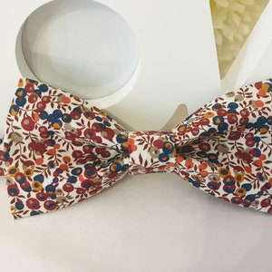 Op de afbeelding: Een strik met een witte achtergrond en een bloemenpatroon in tinten rood, oranje, blauw en bruin.