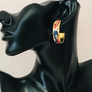 Puede incluir: Pendientes de aro dorados con un estampado floral colorido. Los pendientes están en una cabeza de maniquí negra.