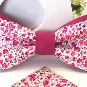 Peut inclure: Un nœud papillon rose avec un motif floral blanc. Le nœud papillon a un centre en satin rose et est fait de coton.