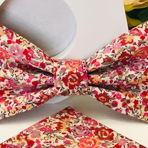 Peut inclure: Un ensemble de nœud papillon et de pochette de poche à motif floral dans des tons de rose, rouge et jaune sur fond blanc.