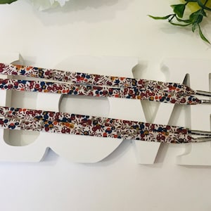 May include: Four pairs of white shoelaces with a floral pattern in shades of red, blue, and brown. The shoelaces are displayed on a white wooden sign that says "LOVE".