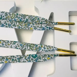 May include: Shoelaces with a floral pattern in shades of blue, green, and yellow. The shoelaces have gold-colored aglets. The background is a white surface with the letters "LOVE" in white.