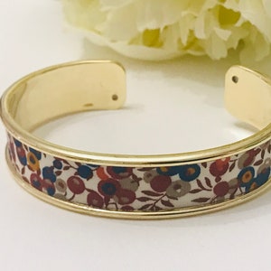Peut inclure: Un bracelet jonc en or avec un bandeau en tissu blanc orné d'un motif floral dans les tons rouge, bleu et marron.