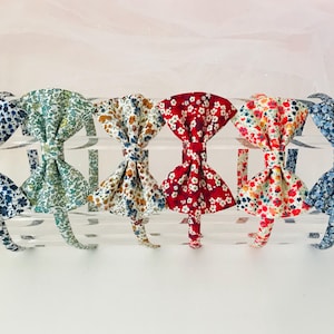 Könnte beinhalten: Sechs Blumenmuster-Stoff-Haarreifen mit Schleifen-Akzenten. Die Haarreifen sind in verschiedenen Farben, darunter Blau, Grün, Weiß, Braun, Rot und Orange.